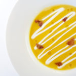 plated butternut squash soup with creme fraiche, candied bacon bits and rosemary oil