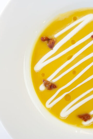 plated butternut squash soup with creme fraiche, candied bacon bits and rosemary oil