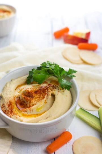 A bowl of hummus drizzled with olive oil and a dash of paprika surrounded with scattered veggies.