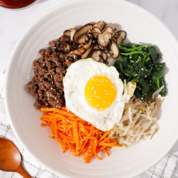 Bibimbap topped with ground beef, spinach, carrot, bean sprouts, mushrooms, and fried egg.