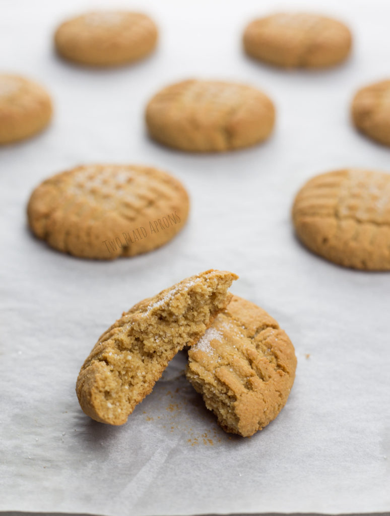 Baked gluten free peanut butter cookies on sheet pan with one cookie split in half.