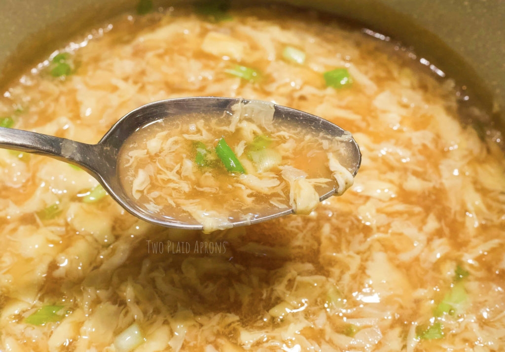 Spoonful of egg drop soup in pot.