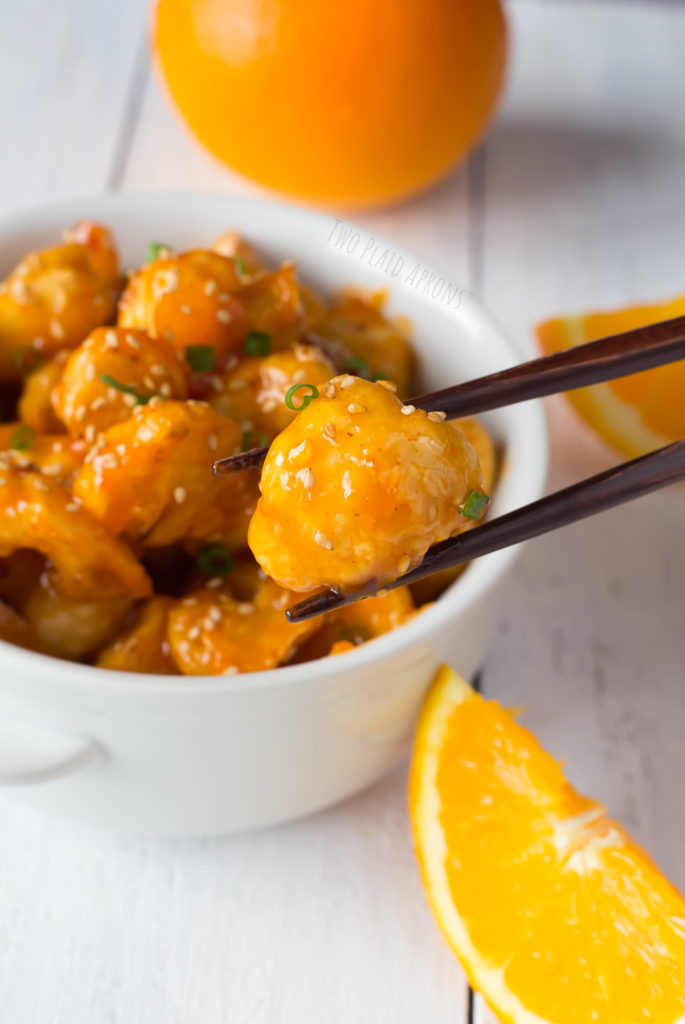 A pair of chopsticks holding a piece of the baked orange cauliflower.