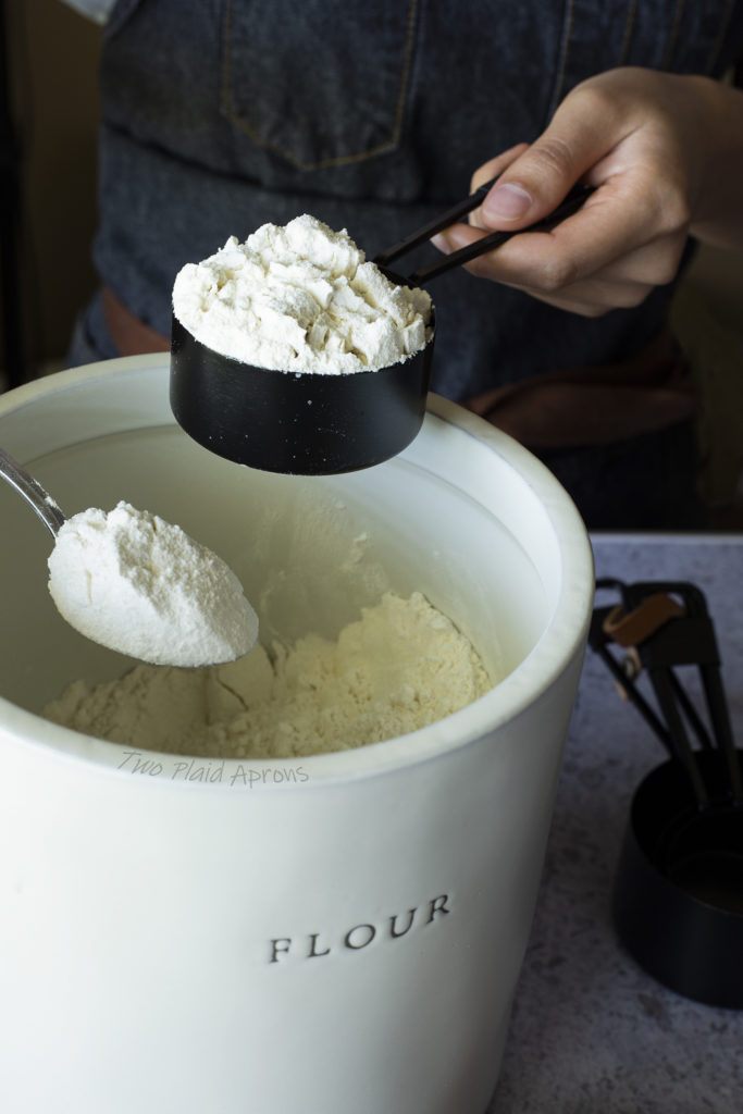 Scooping spoonfuls of flour to fill a measuring cup.