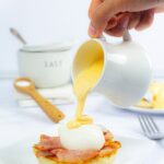 How to make hollandaise: 3 ways - pouring hollandaise on eggs benedict.