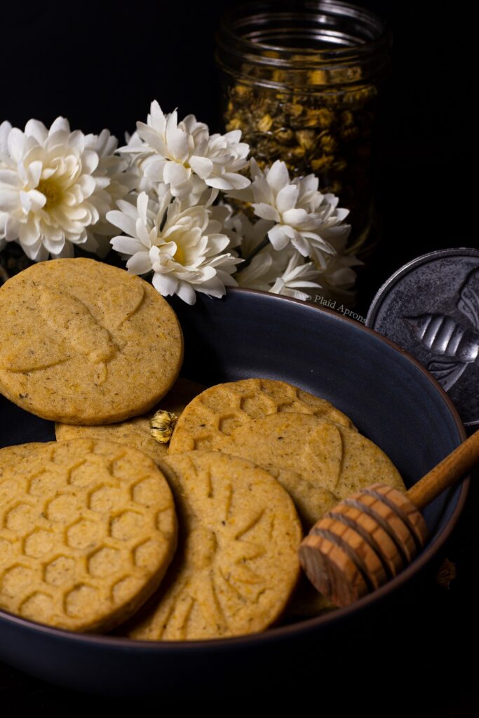 A bowl of honey chrysanthemum shortbread cookies with a honey dipper.