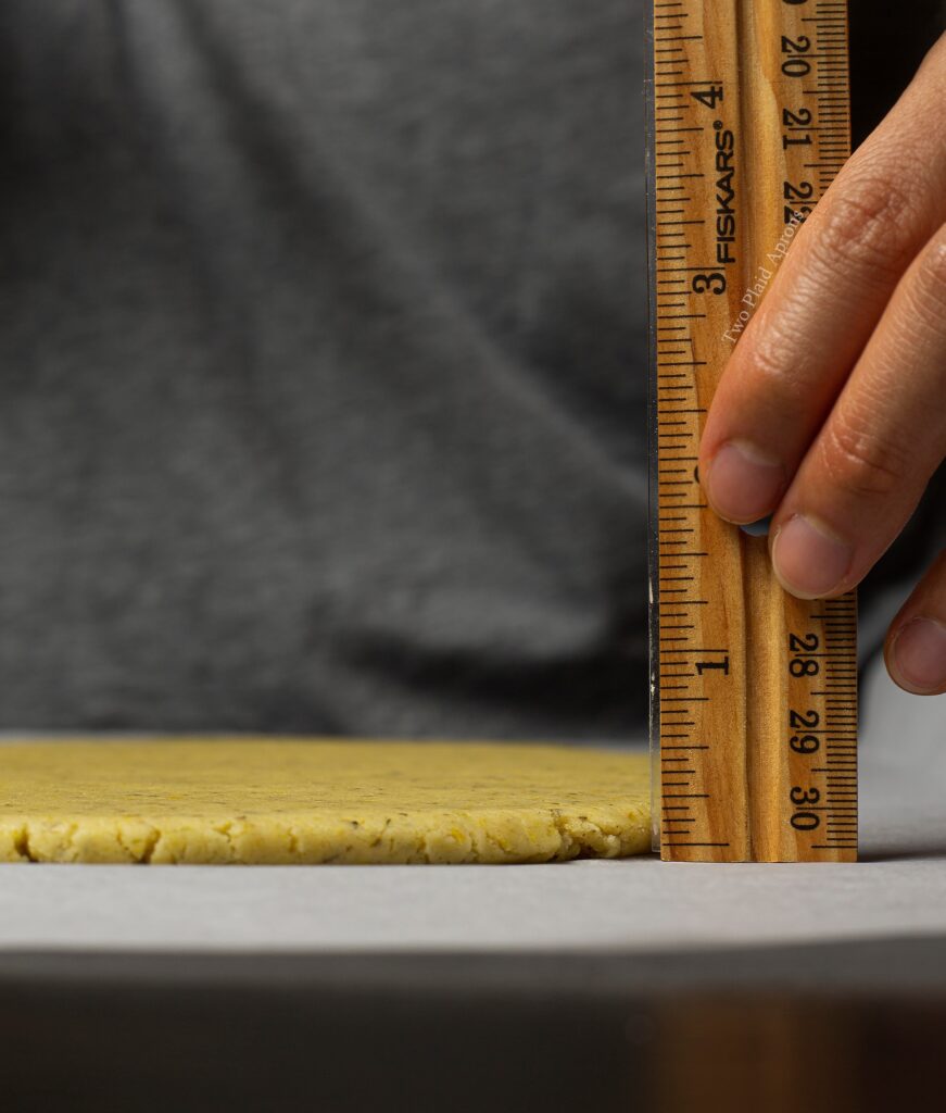 Measuring a sheet of rolled cookie dough with a ruler.