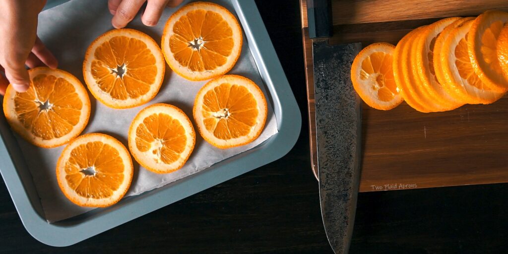 Placing thinly sliced oranges on parchment lined sheet pan.