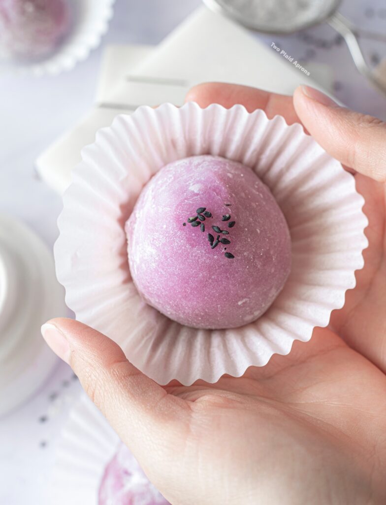 Holding an ube mochi with black sesame filling in a cupcake liner.