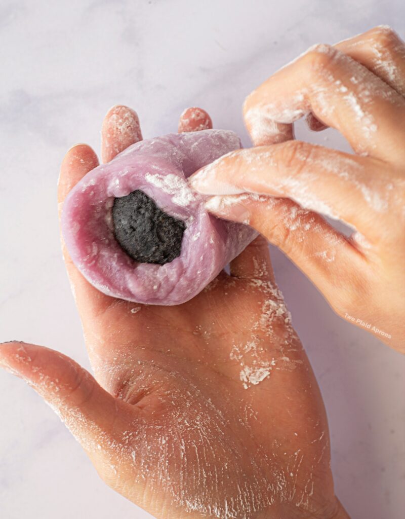 Sealing the black sesame filing in the ube mochi by pinching the edges together.