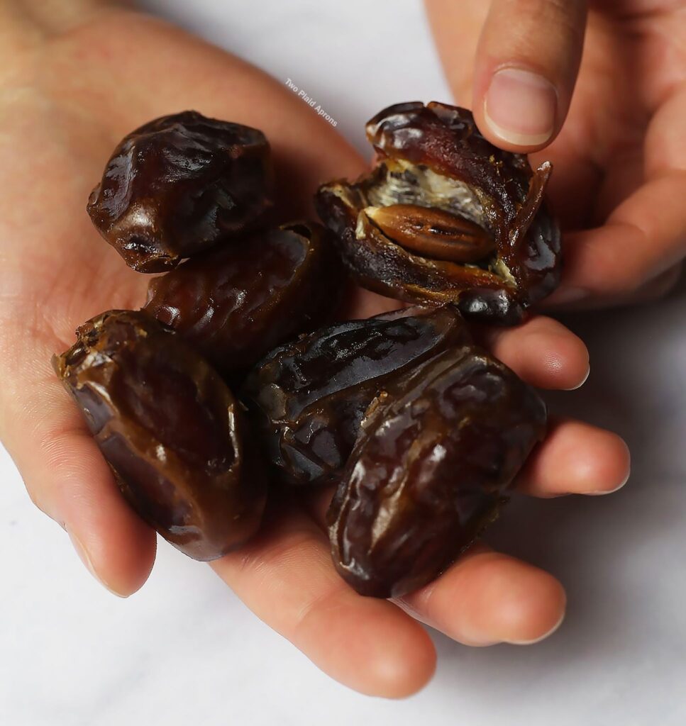 A handful of Medjool dates with one open to show pit.