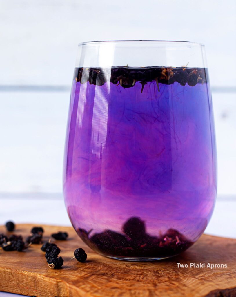 A glass of black wolfberry tea in the process of turning form violet to pinkish purple.