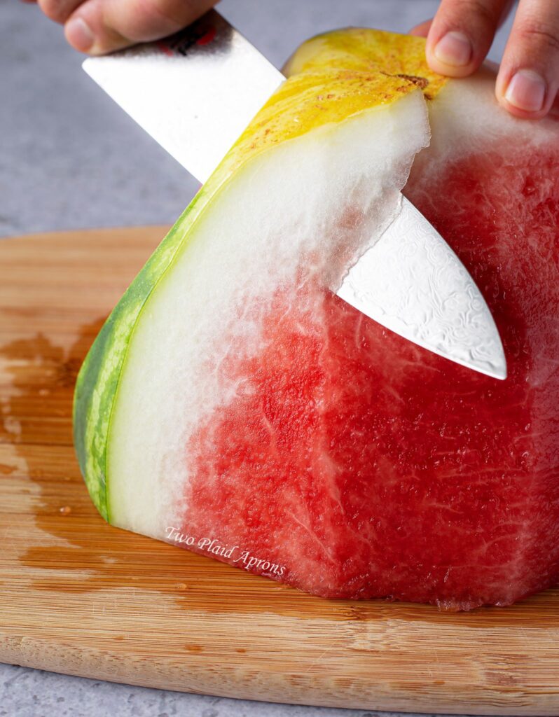 Trimming away watermelon rind with a knife.