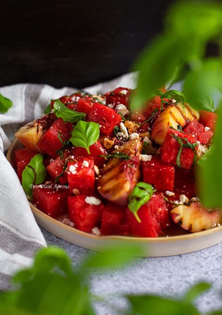 A platter of the watermelon and grilled peach salad seen through a bunch of basil.