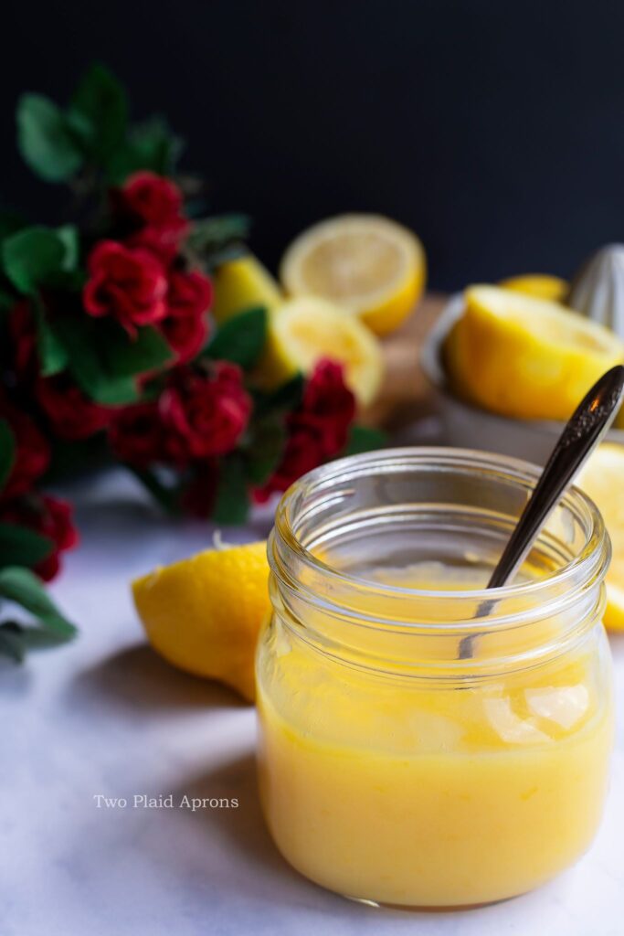 Front view of a jar of lemon curd with a spoon in it.