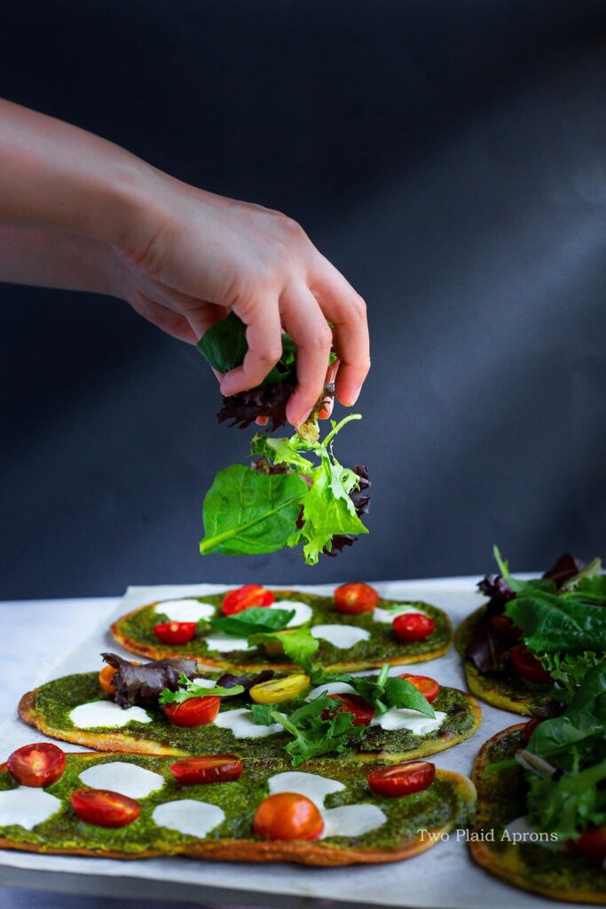 Sprinkling mixed greens onto baked spinach pesto flatbread.