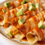 Close up angled shot of Instant Pot chicken taquitos with sauce and diced avocado.