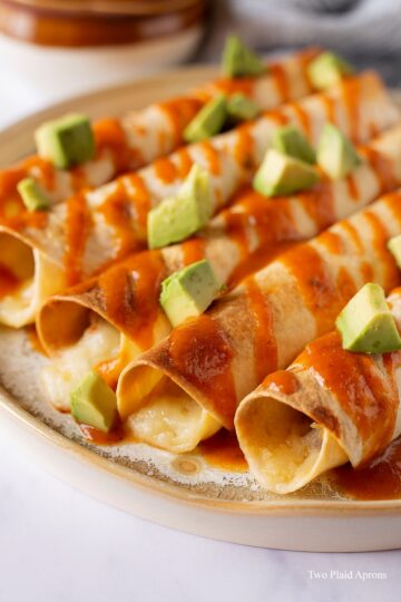 Close up angled shot of Instant Pot chicken taquitos with sauce and diced avocado.