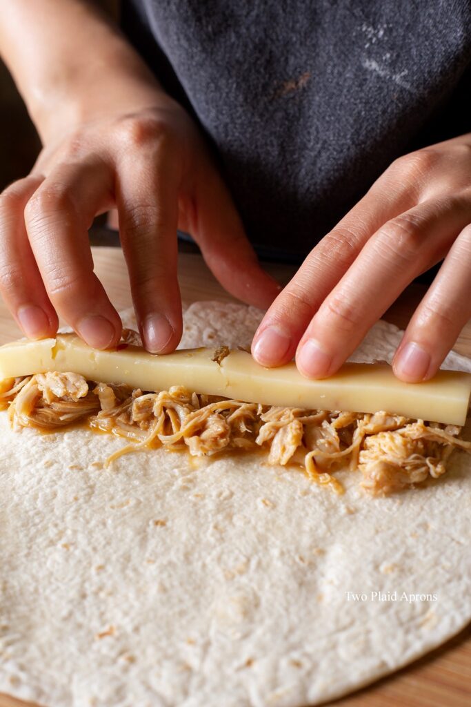 Layering and lining the tortilla with chicken and cheese for rolling.