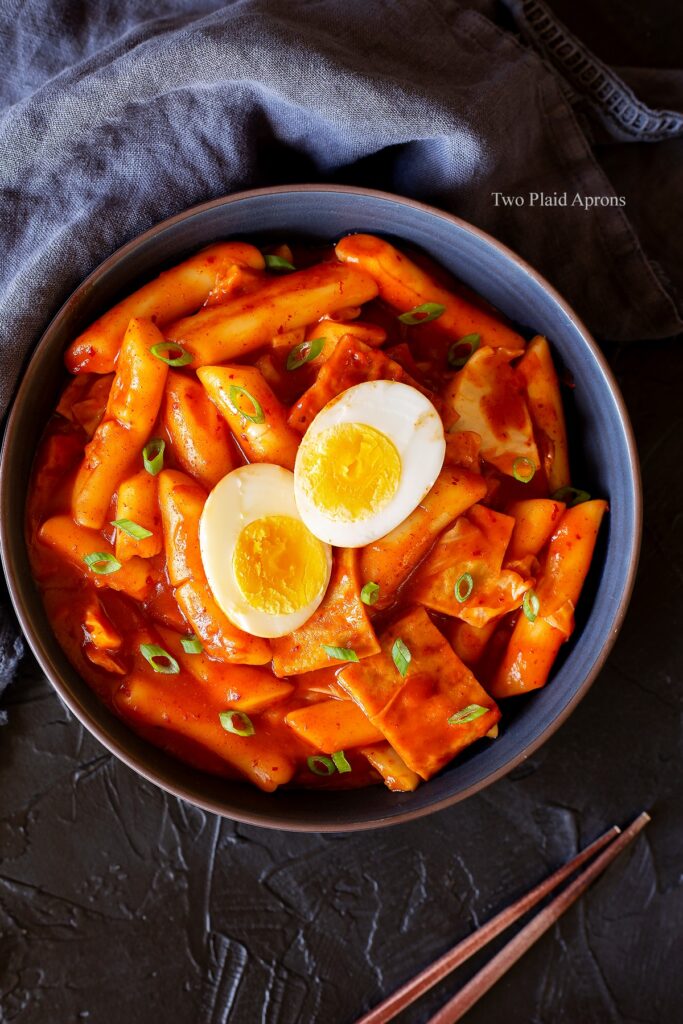 Top down, wide view of a bowl of tteokbokki with chopsticks on the side.