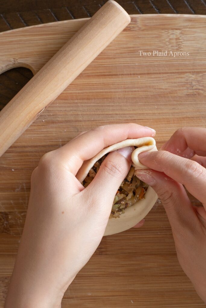 Folding the edge of the bao bun wrapper to pleat.