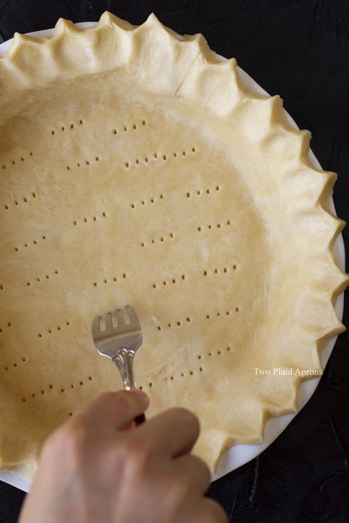 Poking holes on the bottom of the crust with a fork.
