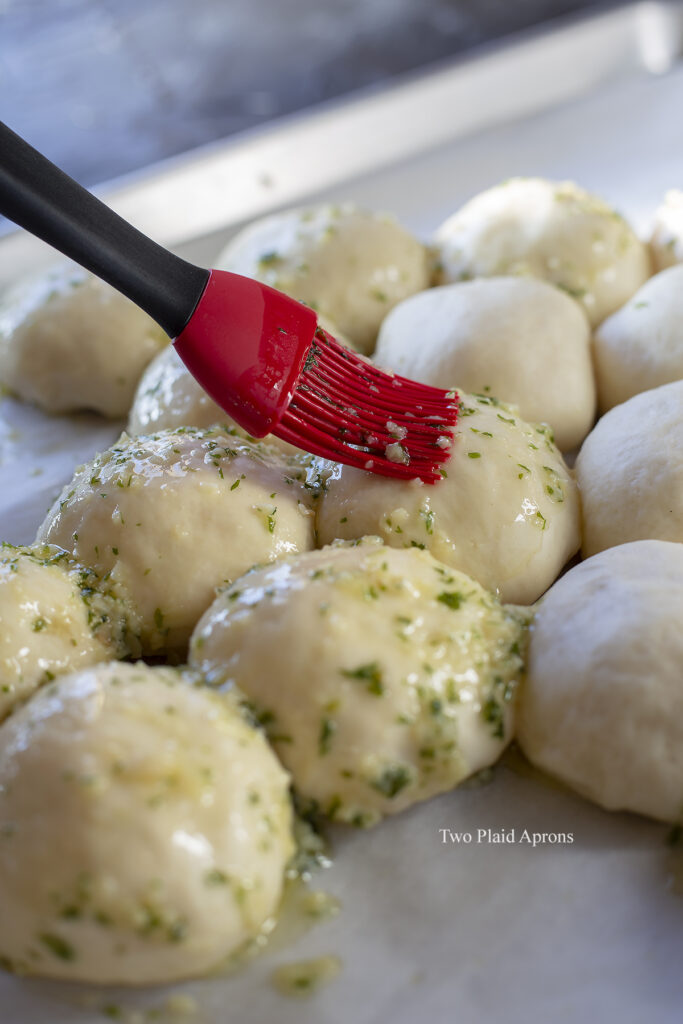 Brushing the garlic butter onto the rolls with a red brush.