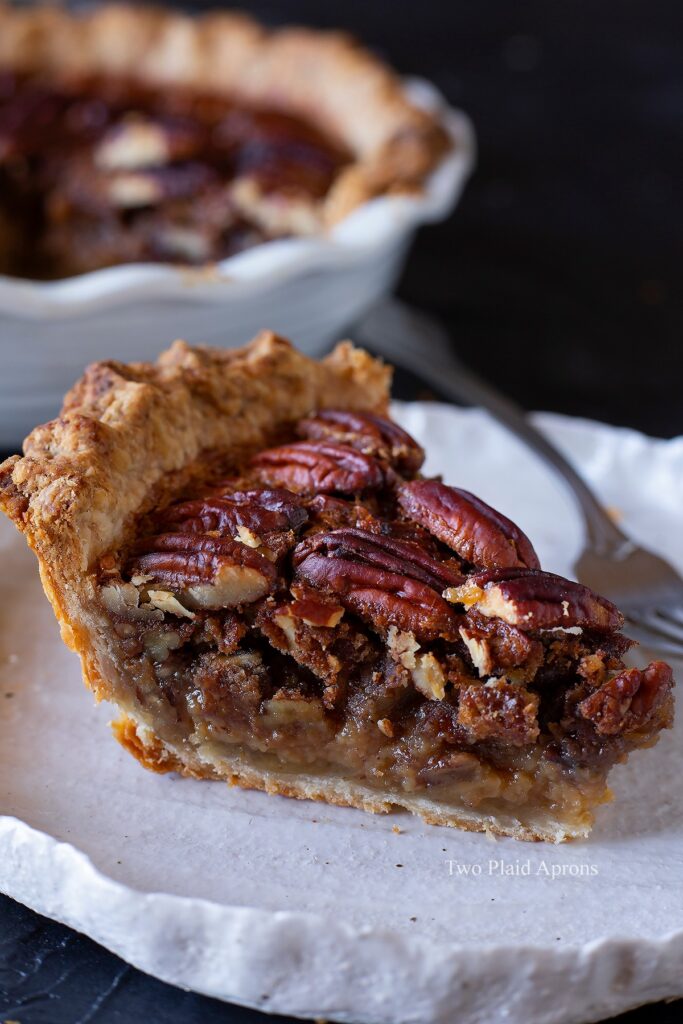 Side view of a slice of maple syrup pecan pie on a plate with fork.