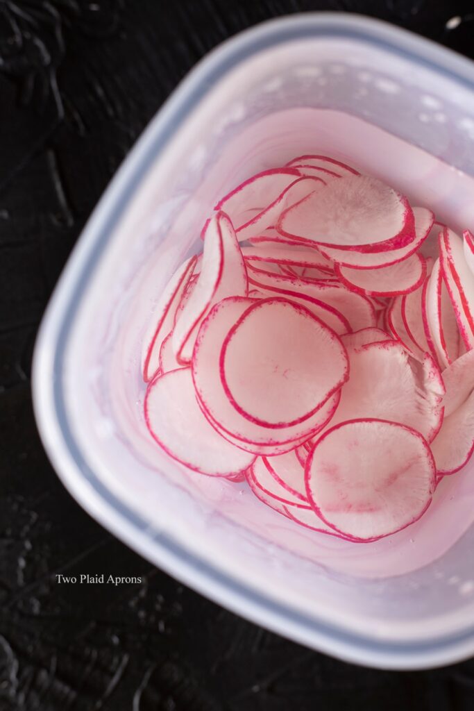 Top down view of the thinly sliced radishes soaking in cold water.
