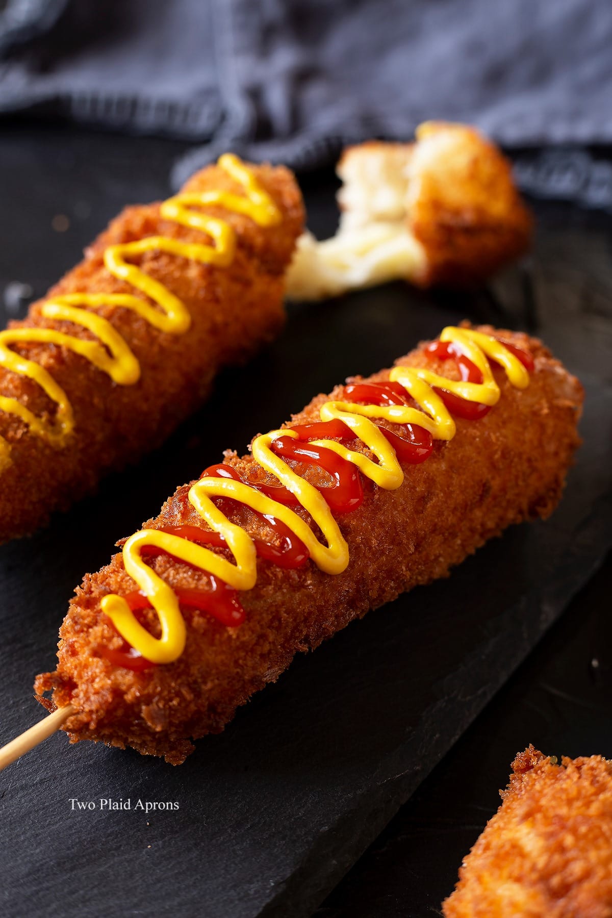 Side view of Korean cheese corn dog dressed with ketchup and mustard on a plate.
