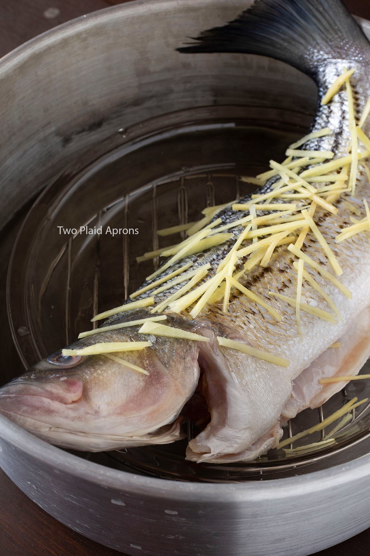A whole striped bass topped with julienned ginger, in a pot ready for steaming.