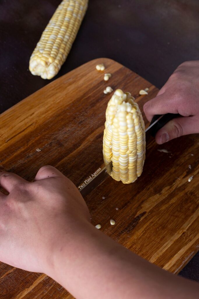 Pushing the blade of the knife down a cob of corn.