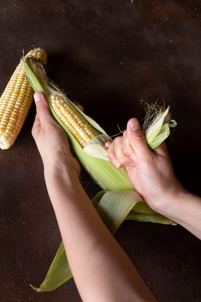 Pulling the husk of the corn down to the base of the cob.