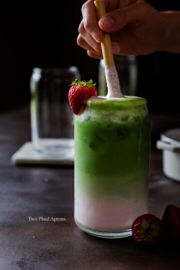 Stirring a glass of strawberry matcha latte with a straw.