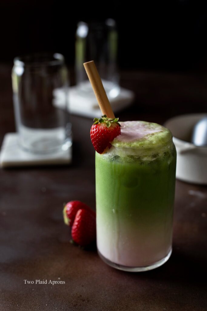 Wide, front view of a glass of strawberry matcha latte garnished with strawberries.