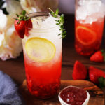 Front angled view of a tall glass of the sparkling strawberry lemonade with a small bowl of strawberry bobas.