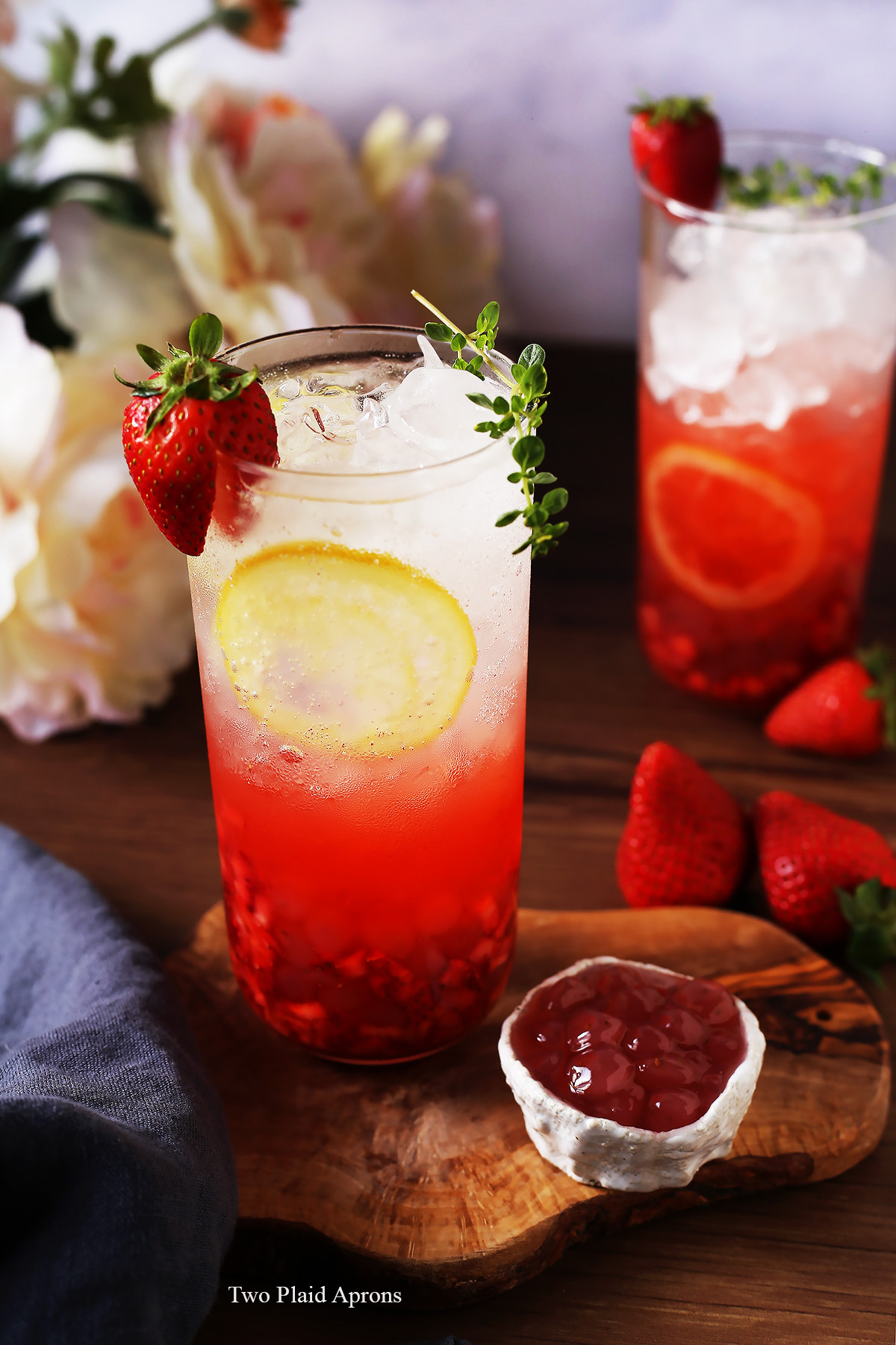 Front angled view of a tall glass of the sparkling strawberry lemonade with a small bowl of strawberry bobas.