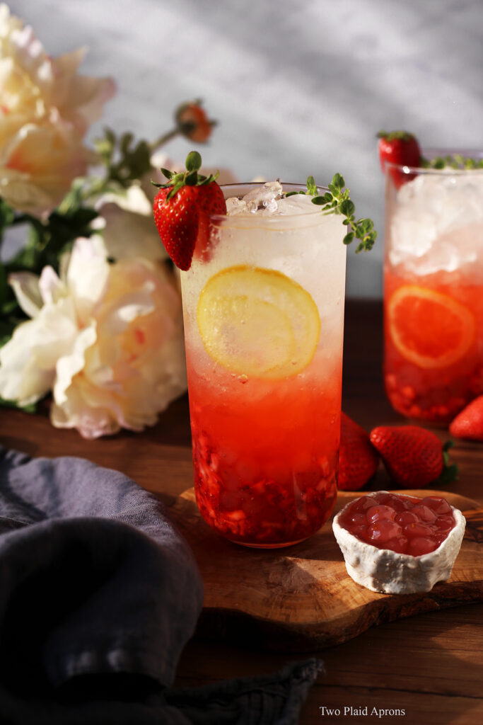 Front view of a glass of sparkling strawberry lemonade with a small bowl of strawberry bobas in sunlight.