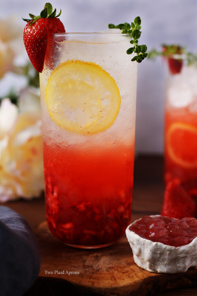 Front view of a glass of sparkling strawberry lemonade garnished with a strawberry and thyme.