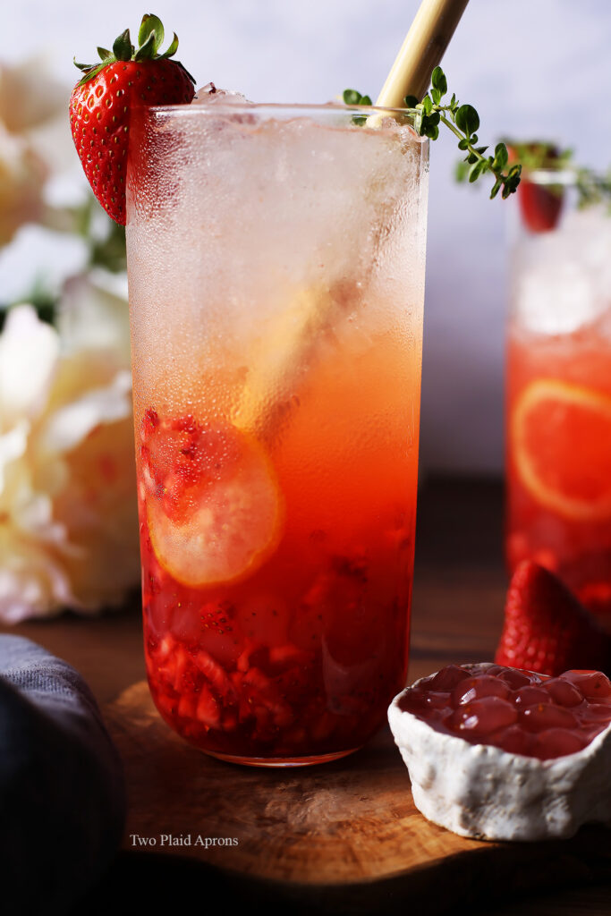 A glass of sparkling strawberry lemonade being stirred with a straw.