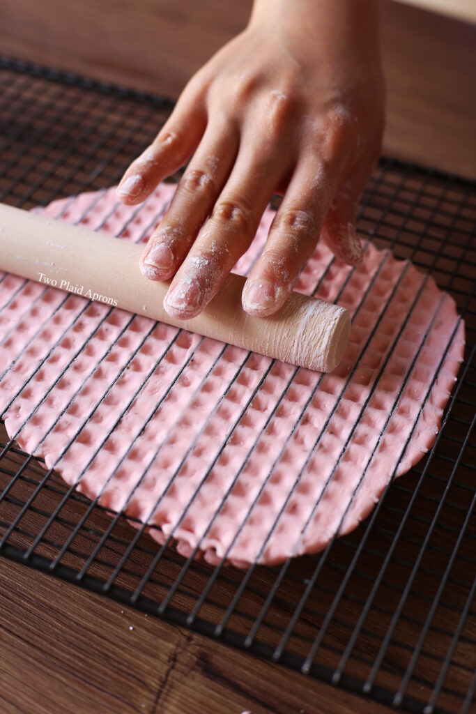 Rolling a slab of fresh strawberry boba dough through a wire rack with a rolling pin.