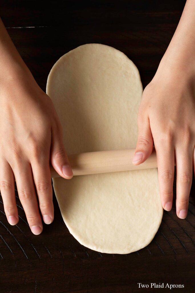 Rolling out the dough into an oblong oval with a rolling pin.