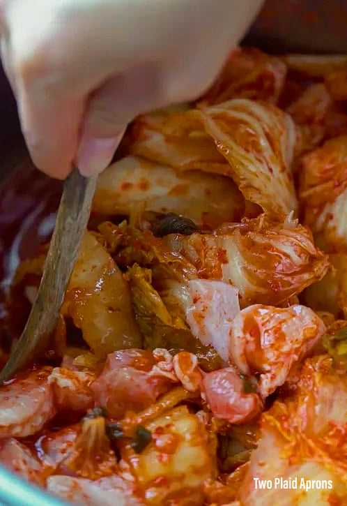 Stirring the kimchi and pork belly together with a spoon.