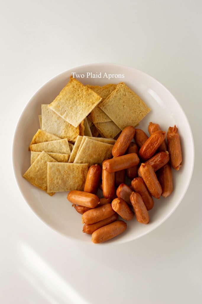 A plate of fish cake sheets cut into squares and sausages with shallow diagonal cuts.