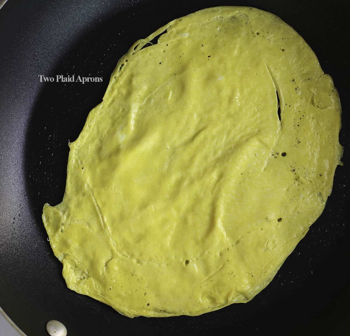 Egg yolk crepe (jidan) cooking in nonstick pan.