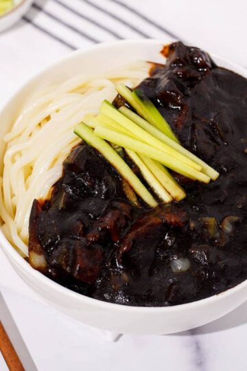 A bowl of jajangmyeon garnished with cucumbers.