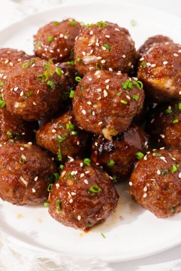 Bulgogi meatballs garnished with green onions and sesame seeds on a plate.