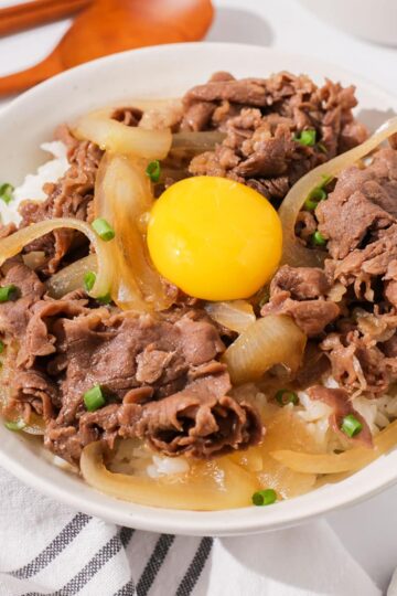 A bowl of gyudon topped with an egg yolk.