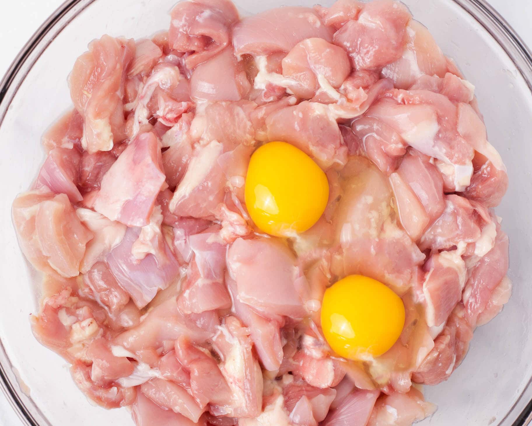 Eggs added to diced chicken thighs in a bowl.