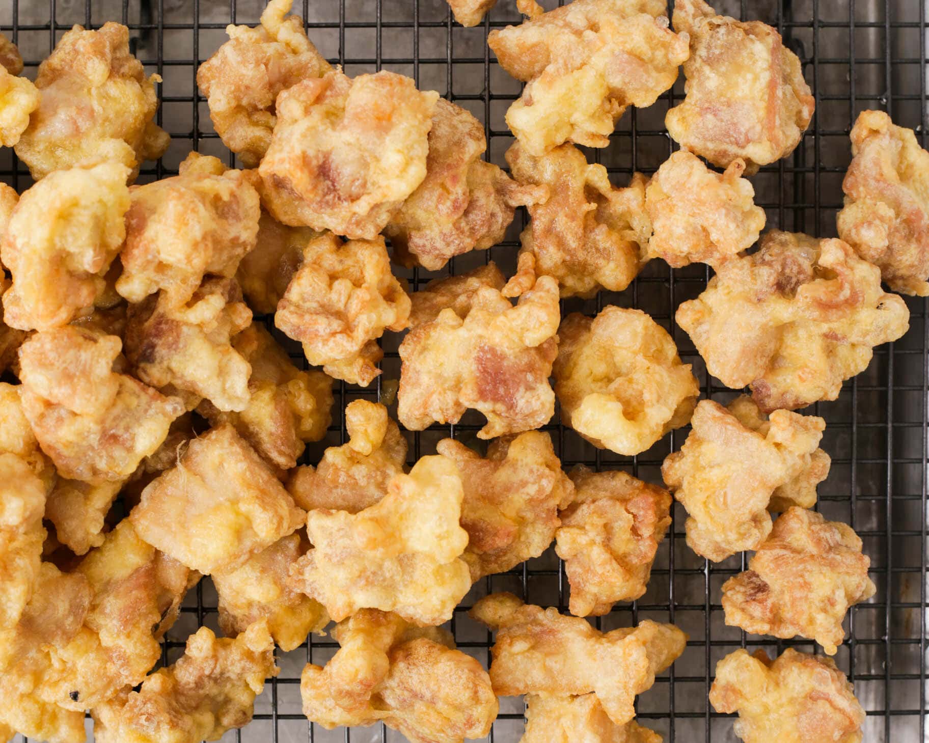 Fried chicken pieces draining on a rack after the first fry.
